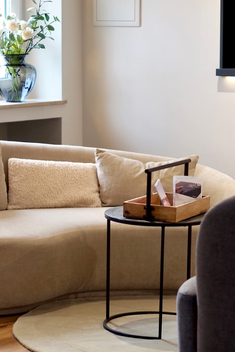 Beige Sofa mit Kissen und einem kleinen Beistelltisch mit Holzablage und dekorativen Objekten.