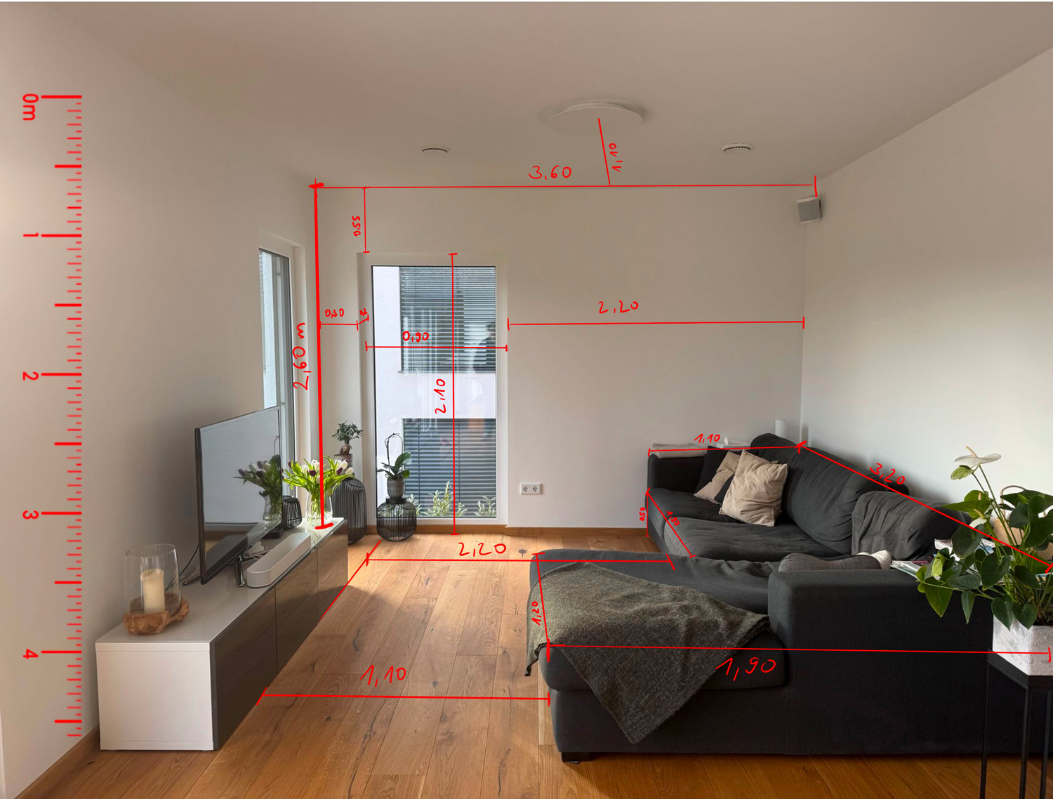 Wohnzimmer mit einem schwarzen Sofa, einem Fernseher und Pflanzen im Raum.